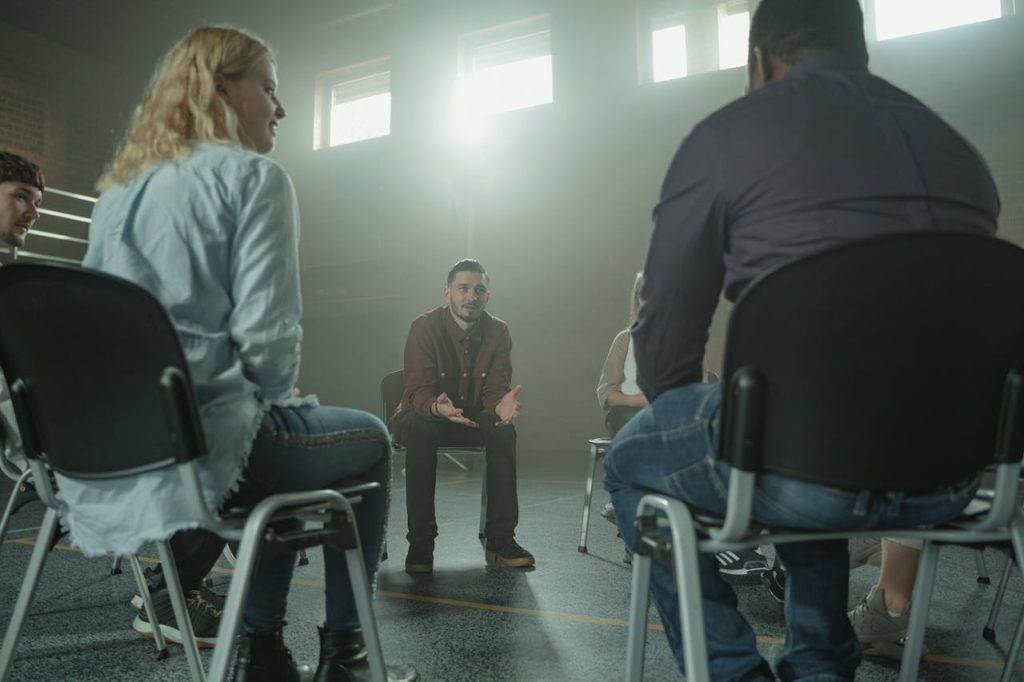 A diverse group of adults in a supportive discussion setting indoors with sunrays.